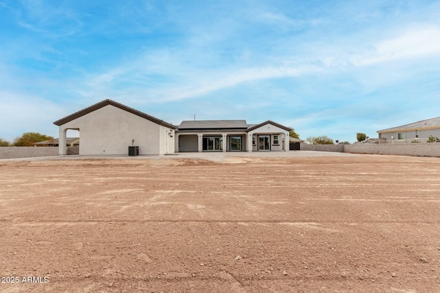back of property with cooling unit, stucco siding, and solar panels