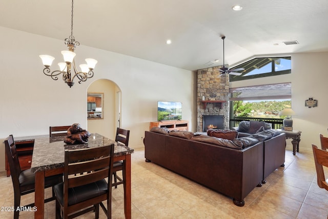 living room featuring lofted ceiling, arched walkways, a stone fireplace, ceiling fan with notable chandelier, and visible vents