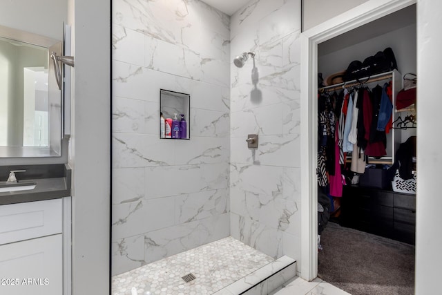 full bath featuring a walk in closet, tiled shower, and vanity