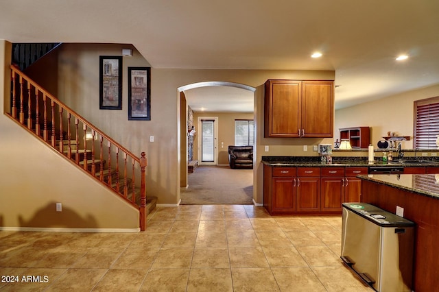 kitchen with light tile patterned flooring, dark stone countertops, and black dishwasher