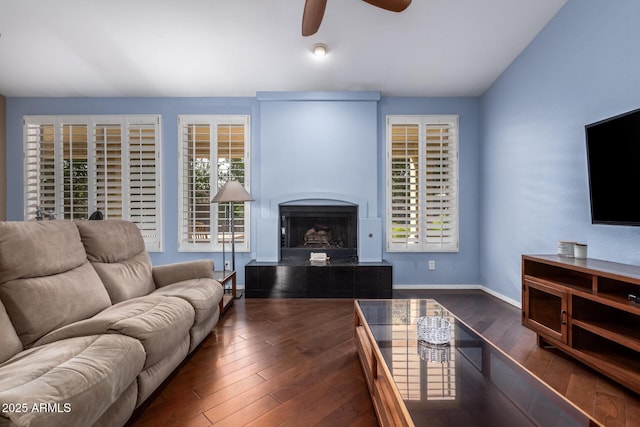 living room featuring baseboards, a fireplace with raised hearth, ceiling fan, wood-type flooring, and vaulted ceiling