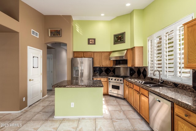 kitchen featuring arched walkways, visible vents, appliances with stainless steel finishes, a sink, and wall chimney exhaust hood