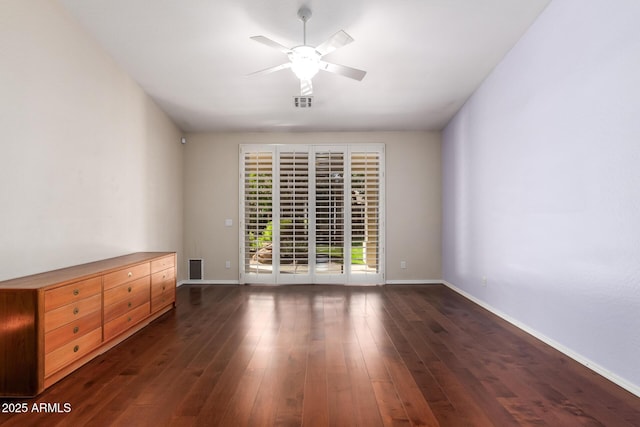 empty room with visible vents, dark wood finished floors, a ceiling fan, and baseboards