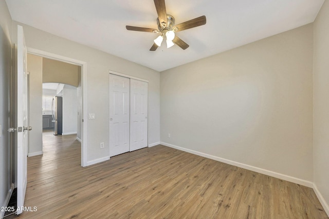 166 W Merrill Ct, Gilbert, AZ 85233 - unfurnished bedroom with arched walkways, light wood-style flooring, a closet, freestanding refrigerator, and ceiling fan