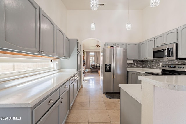 kitchen featuring appliances with stainless steel finishes, hanging light fixtures, gray cabinetry, light tile patterned floors, and a high ceiling