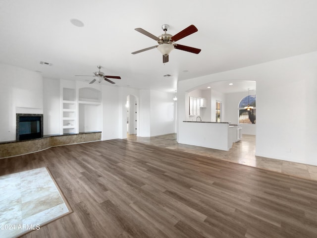 unfurnished living room with ceiling fan, built in features, and hardwood / wood-style floors