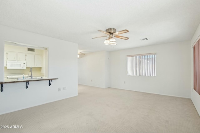 unfurnished living room with light colored carpet, ceiling fan, and sink