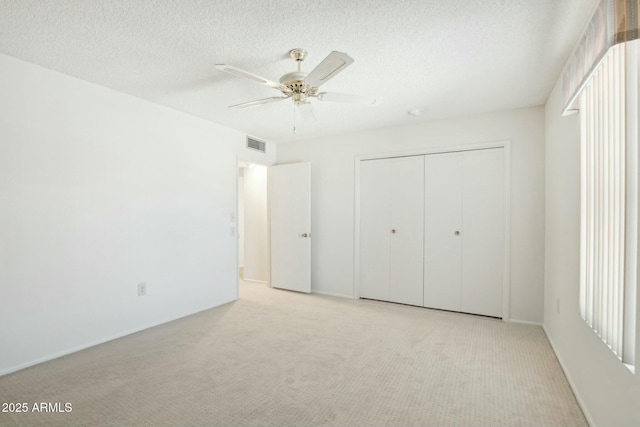 unfurnished bedroom featuring a textured ceiling, a closet, ceiling fan, and light colored carpet