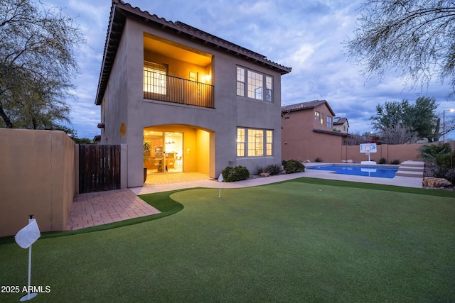 rear view of property with a fenced in pool, stucco siding, a balcony, a fenced backyard, and a patio area