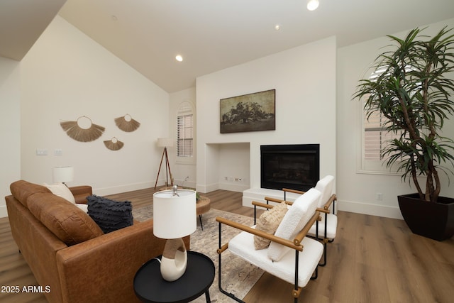 living area with baseboards, lofted ceiling, recessed lighting, wood finished floors, and a glass covered fireplace