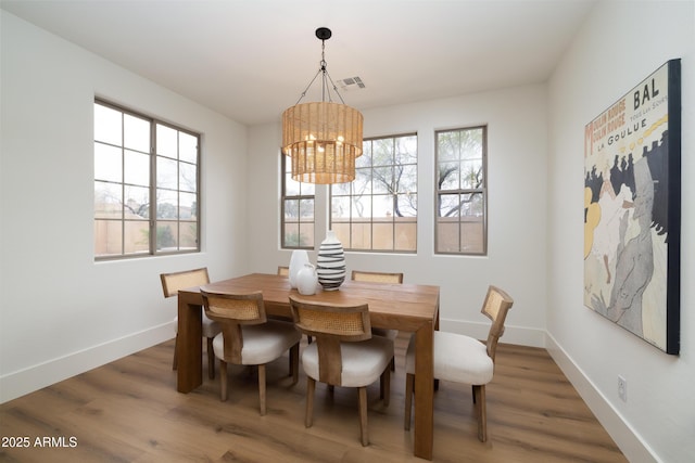 dining space featuring a notable chandelier, wood finished floors, visible vents, and baseboards