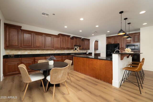 kitchen with visible vents, light wood finished floors, black appliances, a large island, and dark countertops