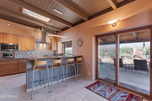 kitchen with appliances with stainless steel finishes, decorative backsplash, wall chimney exhaust hood, a breakfast bar area, and a skylight