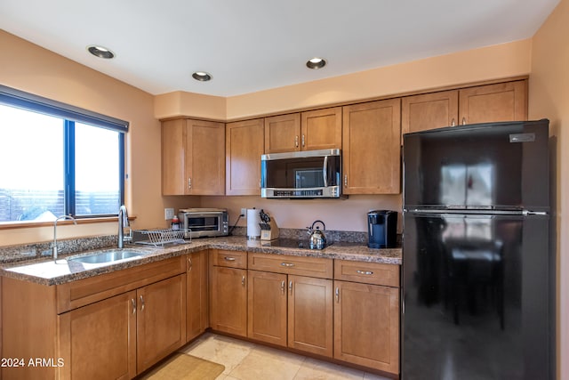 kitchen featuring dark stone counters, sink, light tile patterned floors, and black refrigerator