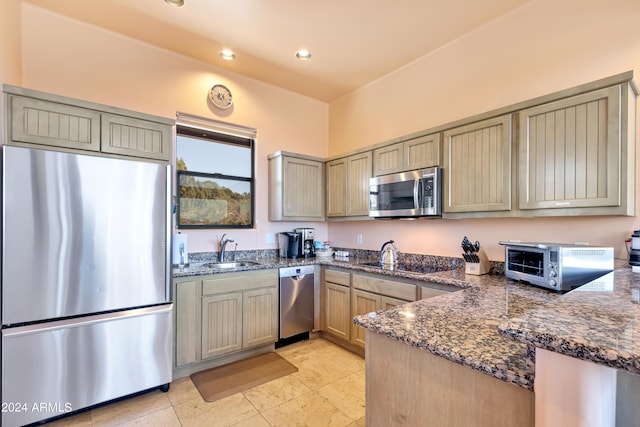 kitchen featuring dark stone countertops, kitchen peninsula, appliances with stainless steel finishes, and sink