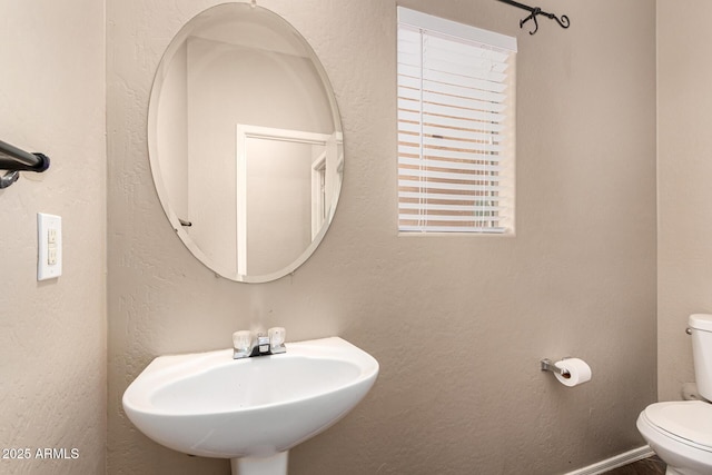 bathroom featuring a textured wall, baseboards, a sink, and toilet