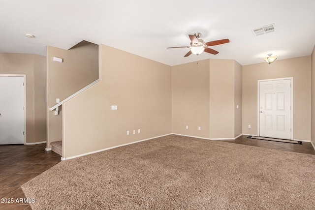 unfurnished room with visible vents, dark carpet, a ceiling fan, dark tile patterned floors, and baseboards