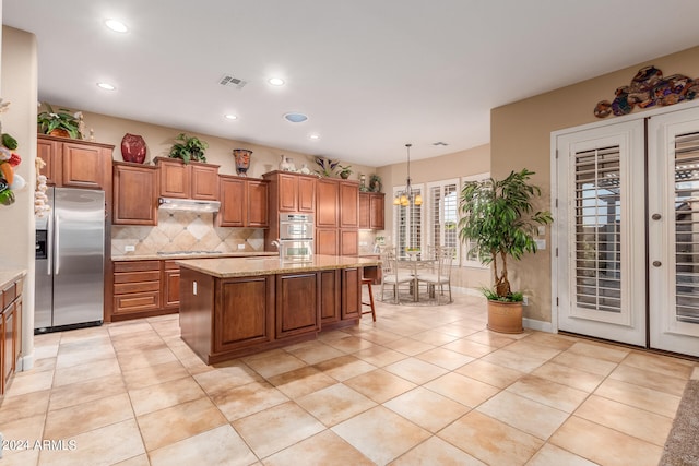 kitchen with appliances with stainless steel finishes, a kitchen island, light tile patterned floors, and decorative light fixtures