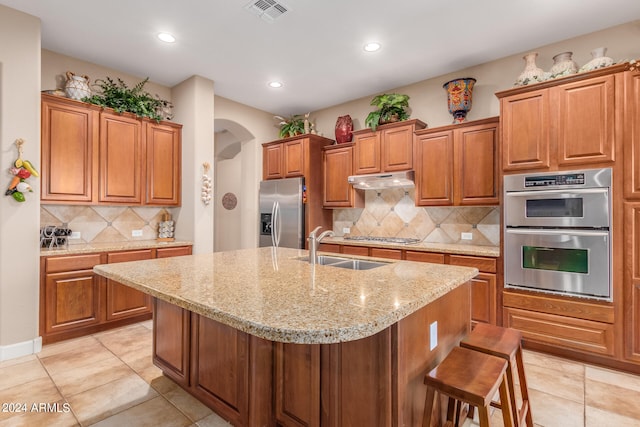 kitchen with an island with sink, backsplash, stainless steel appliances, and a breakfast bar