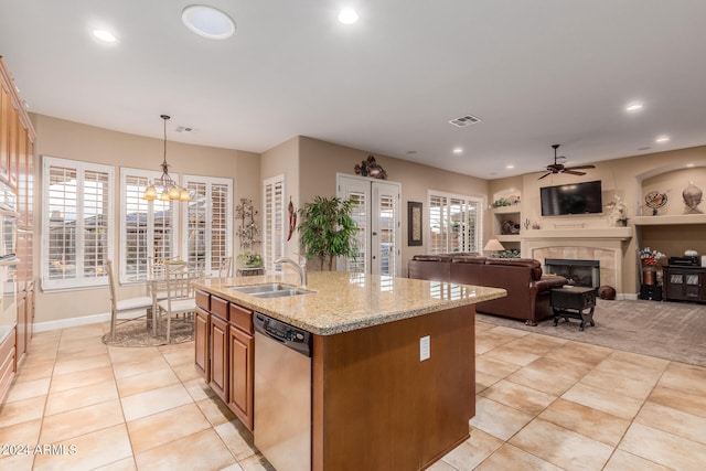 kitchen with an island with sink, stainless steel dishwasher, decorative light fixtures, a tile fireplace, and ceiling fan with notable chandelier