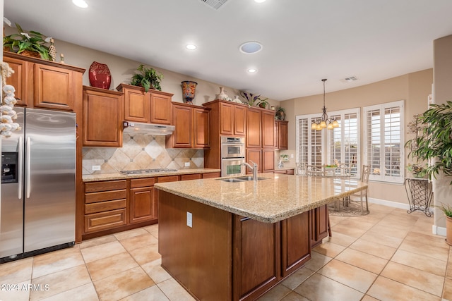 kitchen with an island with sink, light stone countertops, stainless steel appliances, sink, and a chandelier