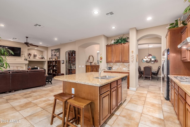 kitchen with sink, ceiling fan with notable chandelier, decorative backsplash, stainless steel appliances, and a center island with sink