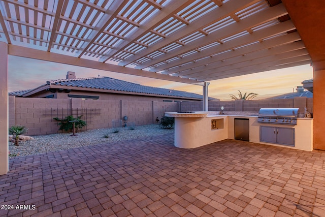 patio terrace at dusk featuring a pergola, area for grilling, and an outdoor kitchen