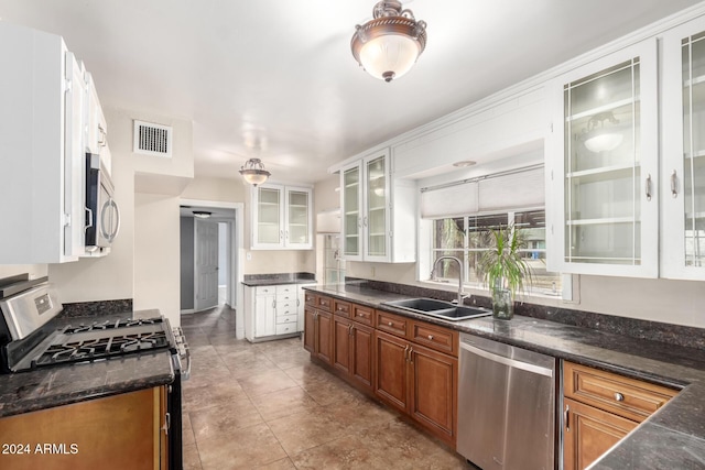 kitchen with sink, light tile patterned flooring, dark stone countertops, white cabinets, and appliances with stainless steel finishes