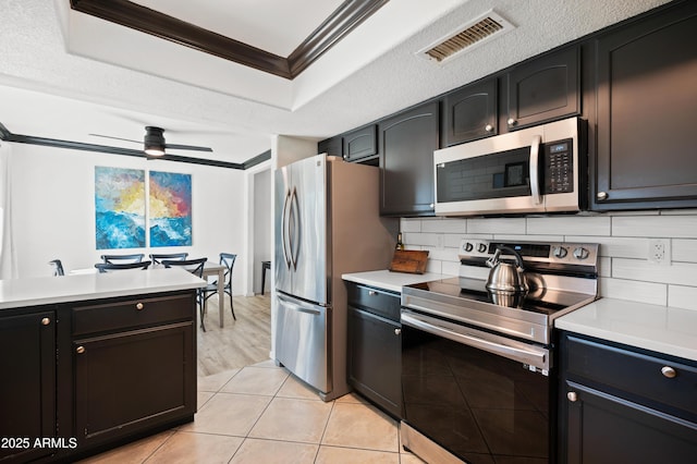 kitchen featuring a raised ceiling, tasteful backsplash, ornamental molding, ceiling fan, and stainless steel appliances