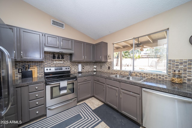 kitchen with gray cabinetry, a sink, visible vents, vaulted ceiling, and appliances with stainless steel finishes