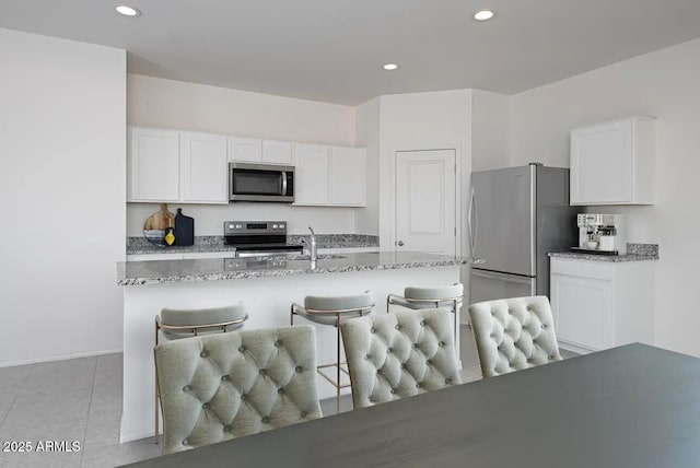 kitchen featuring appliances with stainless steel finishes, a kitchen bar, white cabinetry, and light stone countertops