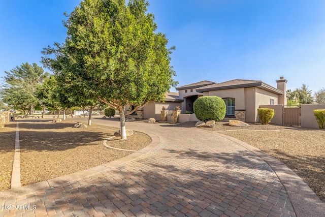 view of front of house featuring stone siding, a gate, fence, decorative driveway, and stucco siding