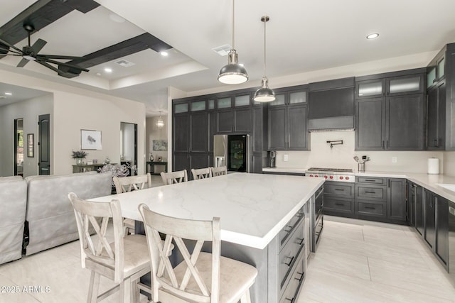 kitchen featuring stainless steel appliances, a kitchen island, custom exhaust hood, light stone countertops, and a kitchen bar