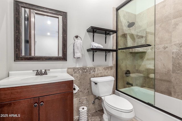 full bath with enclosed tub / shower combo, toilet, vanity, tile walls, and wainscoting