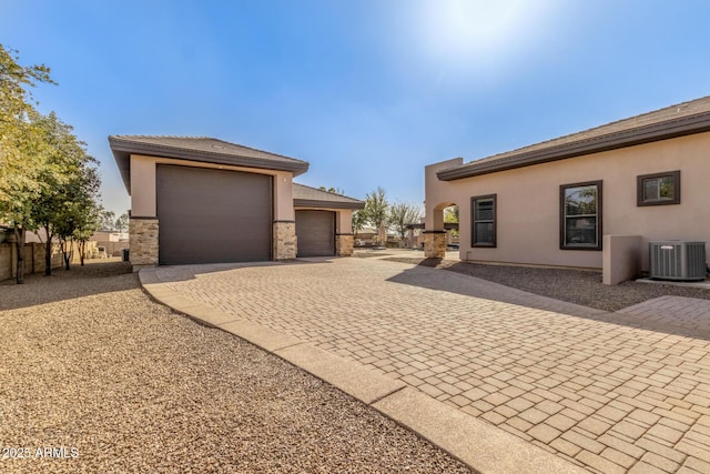 view of property exterior featuring an outbuilding, central AC unit, decorative driveway, and stucco siding