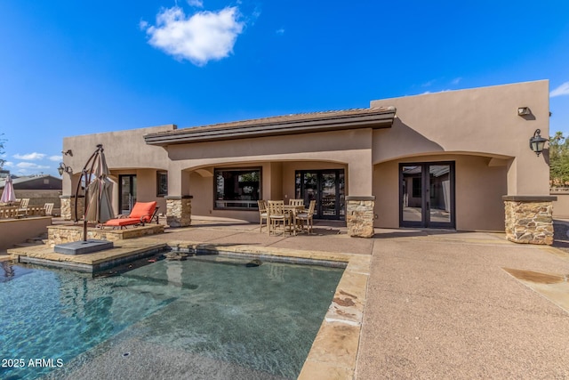 back of house featuring an outdoor pool, an outdoor kitchen, stone siding, a patio area, and stucco siding