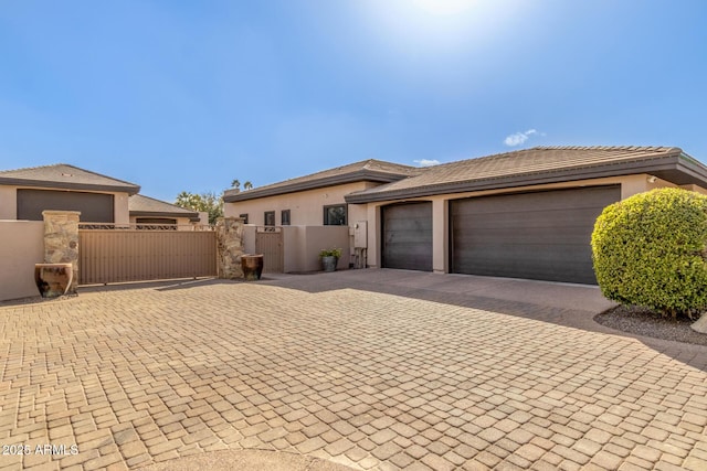 prairie-style home featuring a gate, fence, decorative driveway, and stucco siding