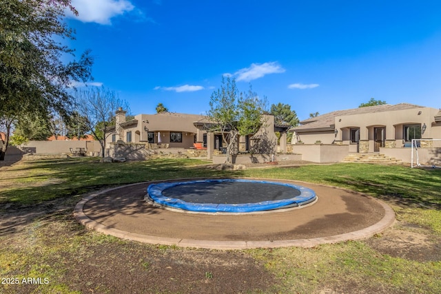 back of property with a trampoline, a yard, fence, and stucco siding