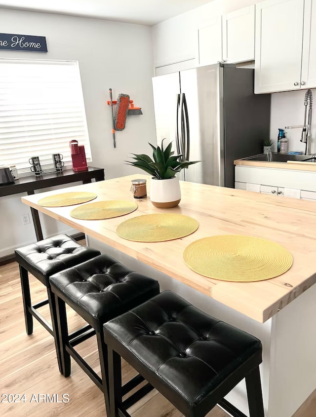 kitchen with a kitchen bar, sink, light hardwood / wood-style floors, white cabinetry, and stainless steel refrigerator