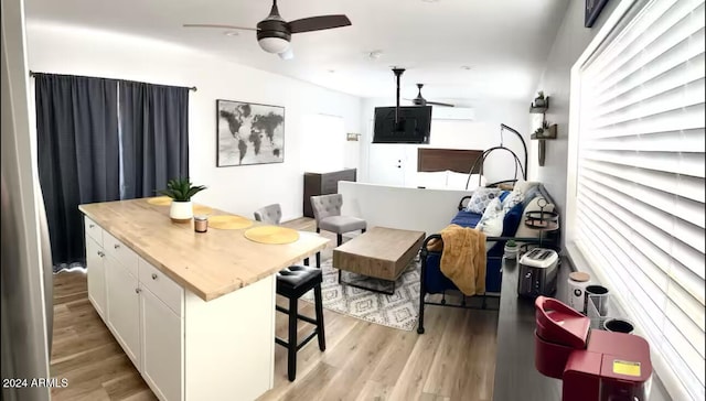 kitchen featuring a kitchen breakfast bar, a wall mounted AC, light hardwood / wood-style flooring, a center island, and white cabinetry