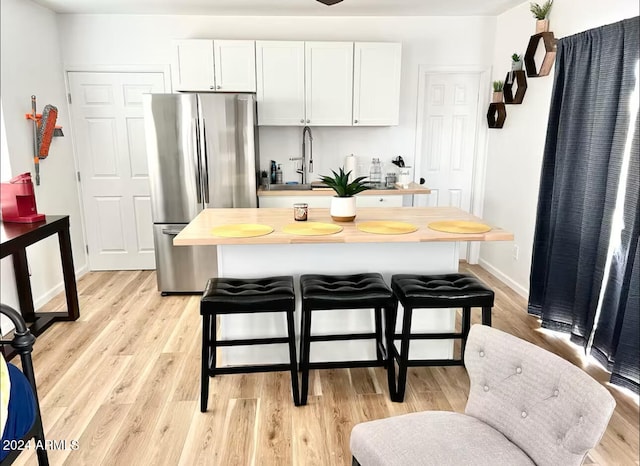 kitchen featuring stainless steel fridge, light wood-type flooring, and white cabinetry