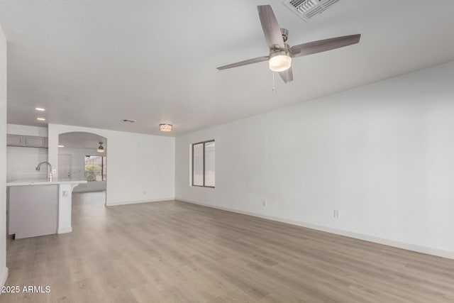 unfurnished living room featuring light wood finished floors, visible vents, arched walkways, a ceiling fan, and a sink