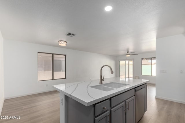 kitchen with visible vents, gray cabinetry, a sink, light stone countertops, and dishwasher