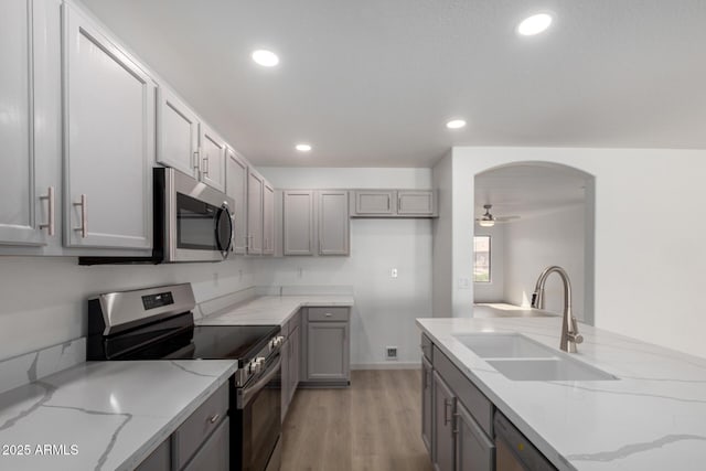 kitchen featuring arched walkways, a ceiling fan, appliances with stainless steel finishes, gray cabinetry, and a sink