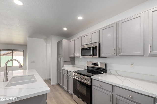 kitchen featuring light wood finished floors, stainless steel appliances, recessed lighting, gray cabinetry, and a sink