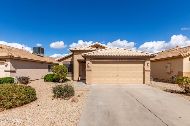 view of front of property featuring a garage, concrete driveway, a tiled roof, central air condition unit, and stucco siding