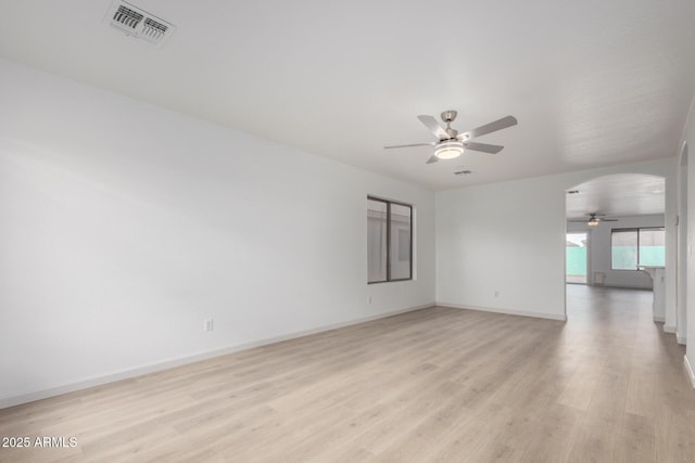 empty room with arched walkways, visible vents, a ceiling fan, light wood-type flooring, and baseboards