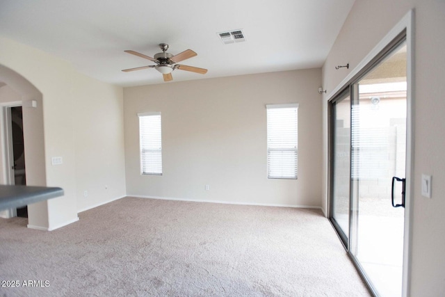 carpeted spare room featuring arched walkways, visible vents, a healthy amount of sunlight, and ceiling fan