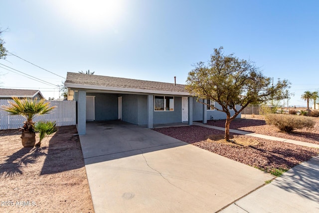 ranch-style home featuring an attached carport, a shingled roof, fence, driveway, and stucco siding