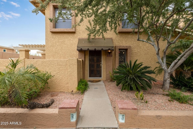 view of exterior entry featuring stucco siding, fence, and a pergola